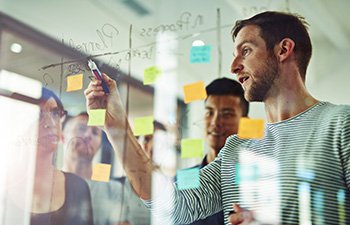 Image of office employees writing on clear dry erase board with post its